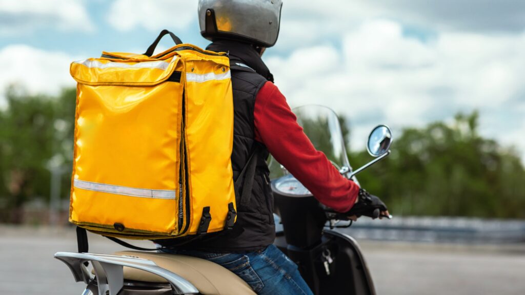 A delivery person on a scooter with a bright yellow insulated backpack, representing Gulfport Food Delivery Accident Attorneys ready to assist in legal cases.