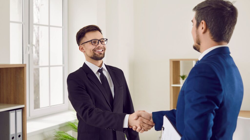 Two men in business suits shaking hands in a bright office setting, symbolizing a successful consultation with Long Beach Personal Injury Lawyers.